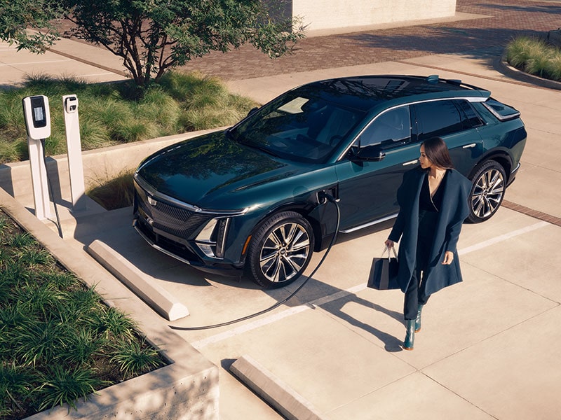 2025 Cadillac LYRIQ EV charging at home as a person walks by.