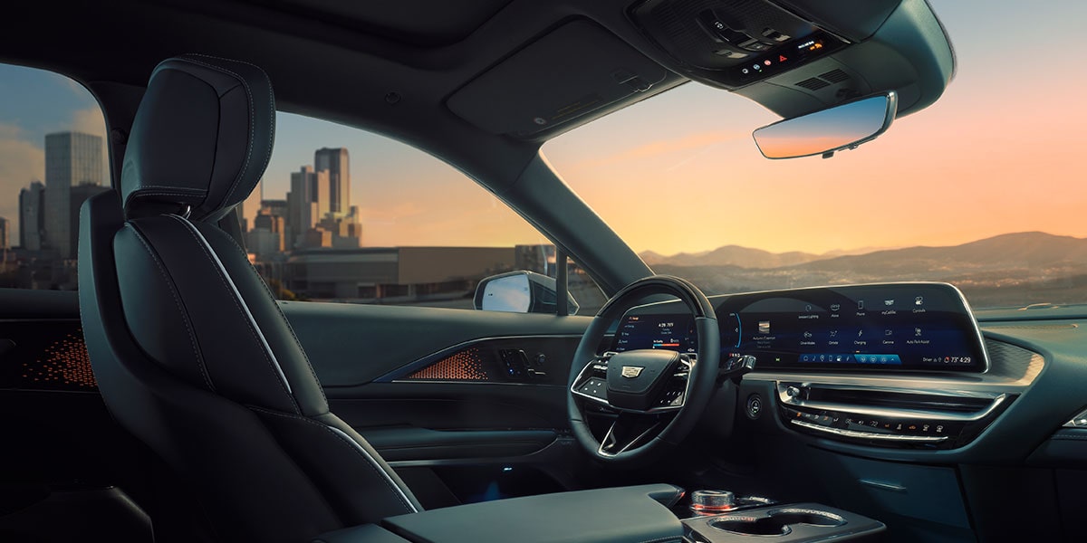 Side view of the front interiors of the 2025 Cadillac LYRIQ parked in a city backdrop.