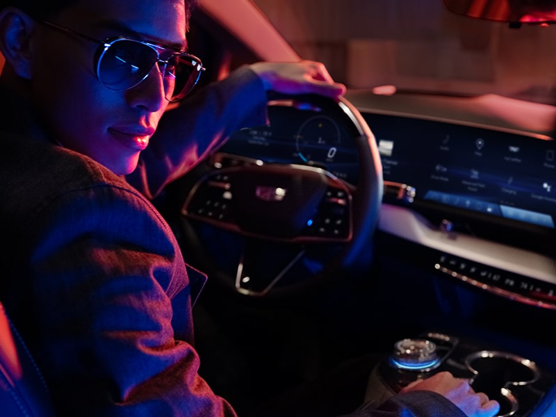 Une personne tient le volant du VUS électrique Cadillac OPTIQ 2025 à une main tout en tournant la tête.