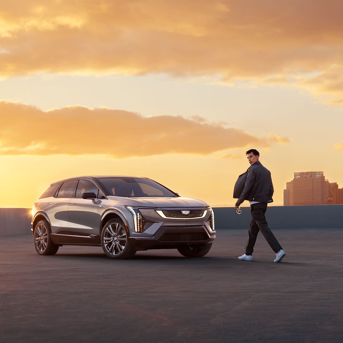 A person passes by the 2025 Cadillac OPTIQ electric SUV parked during sunset.