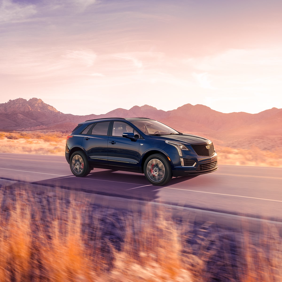 VUS de luxe Cadillac XT5 2025 en mouvement seul sur une route de campagne.