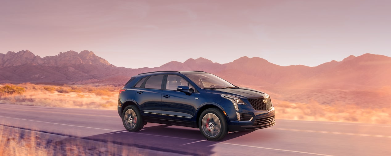 VUS de luxe Cadillac XT5 2025 en mouvement seul sur une route de campagne.