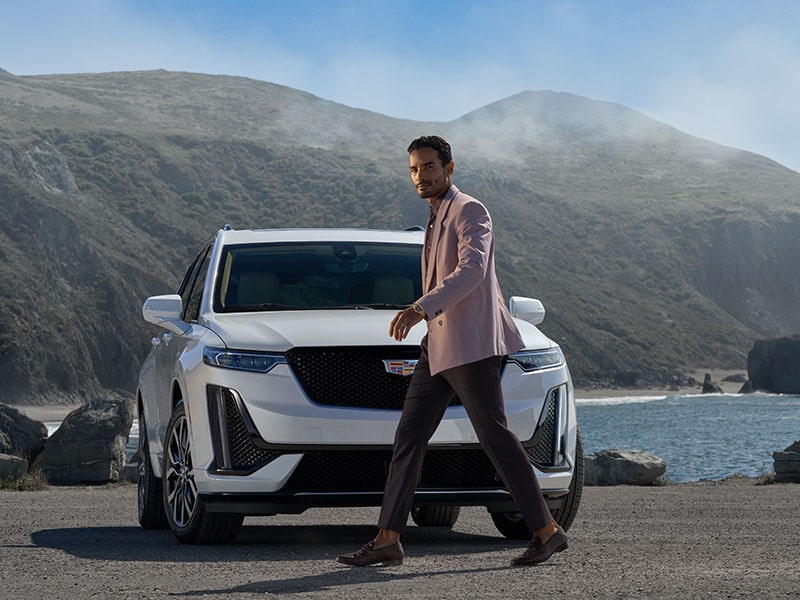 Une personne passe devant un VUS intermédiaire 7 passagers Cadillac XT6 2025 stationné au bord d’un lac.