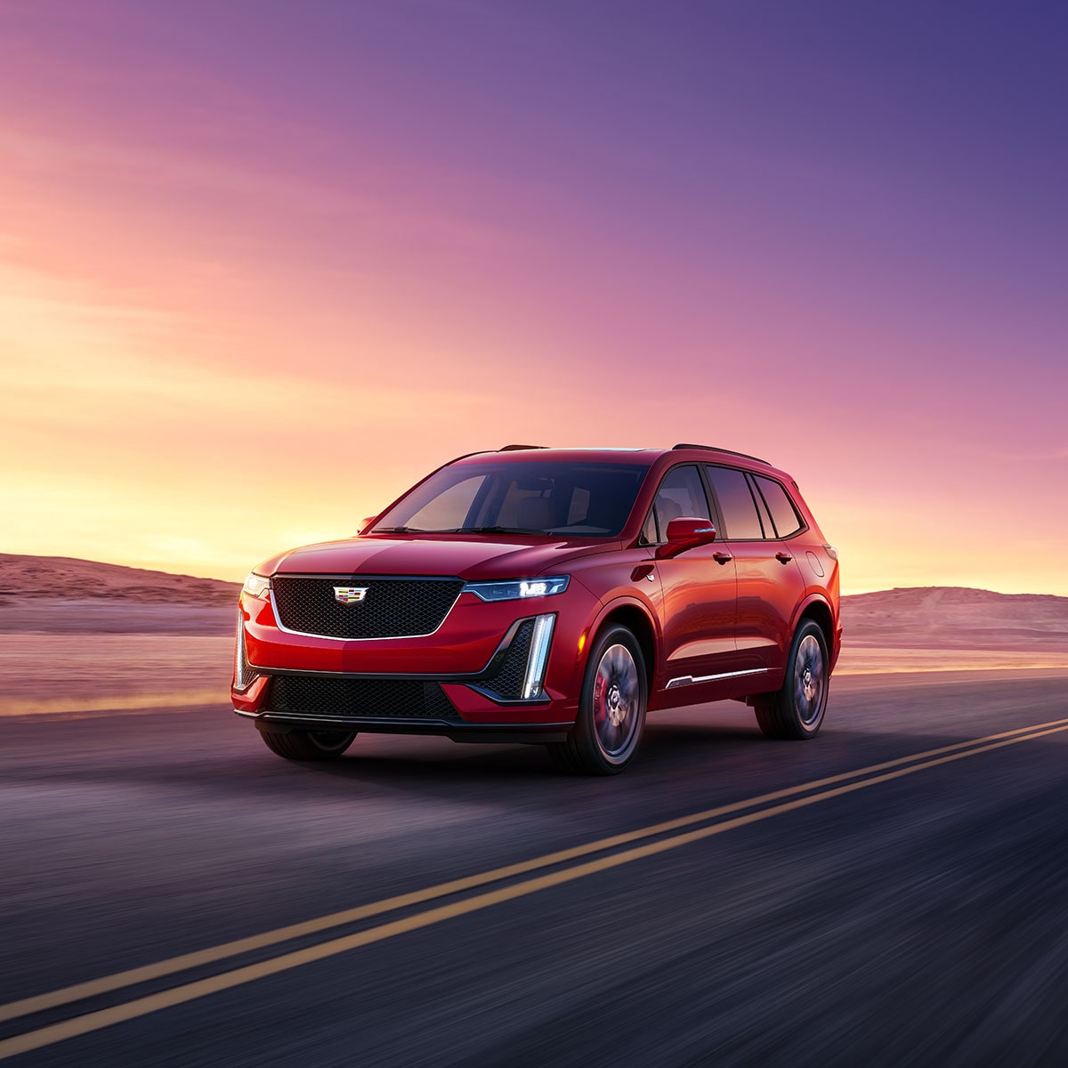 Vue latérale avant du VUS intermédiaire 7 passagers Cadillac XT6 2025 en mouvement seul sur la route au coucher du soleil.