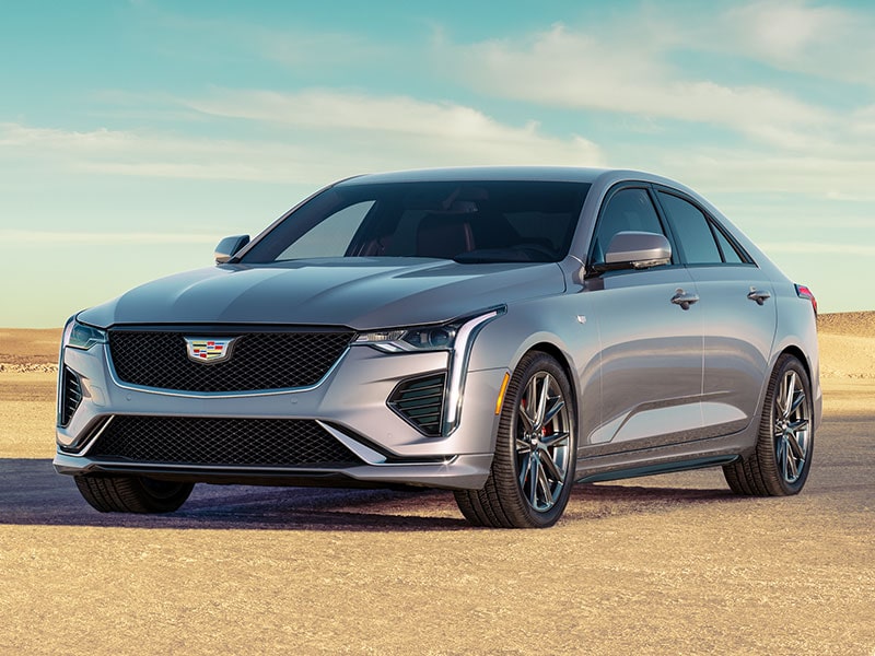 Vue latérale avant de la berline de luxe Cadillac CT4 2025 stationnée seule sur un terrain sablonneux.