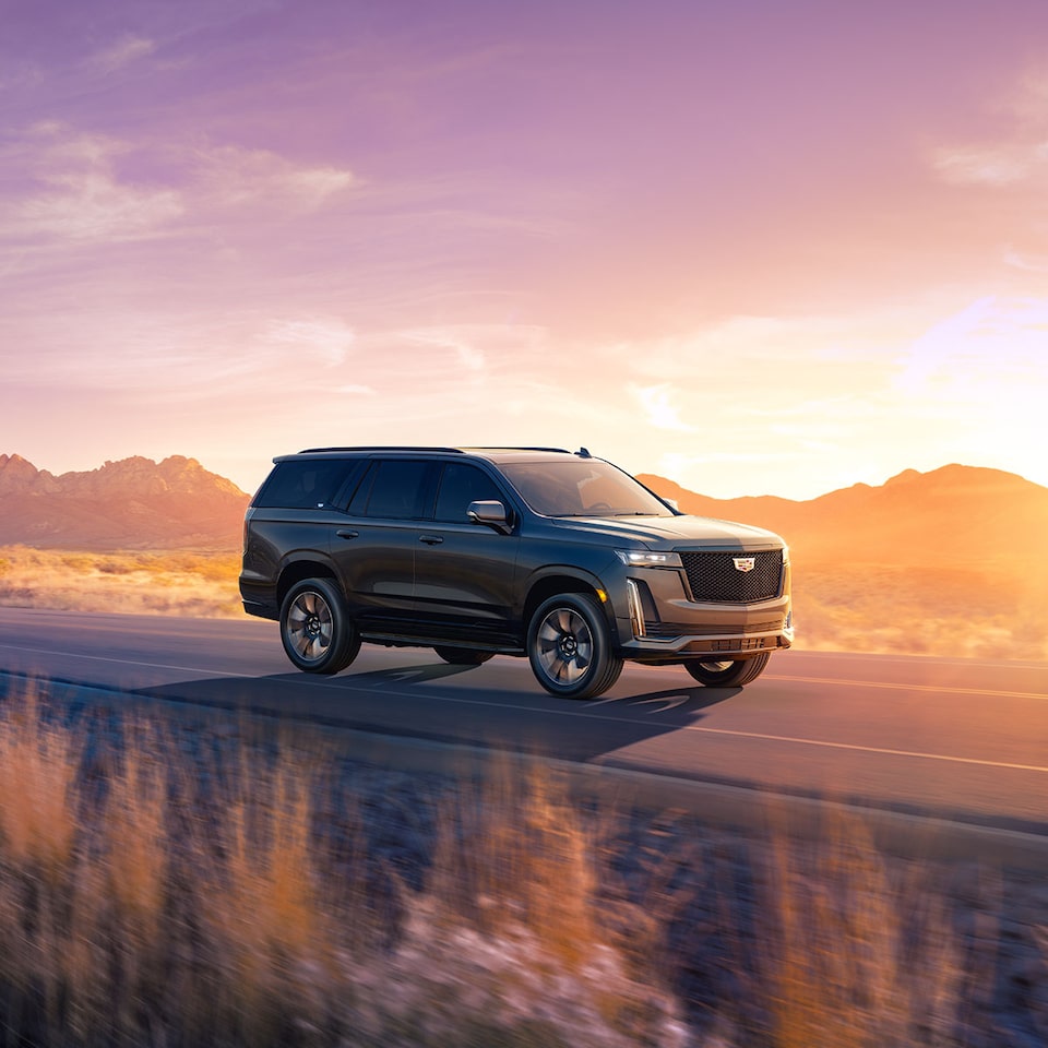 Front right profile view of the 2023 Escalade driving on the road during a sunset.