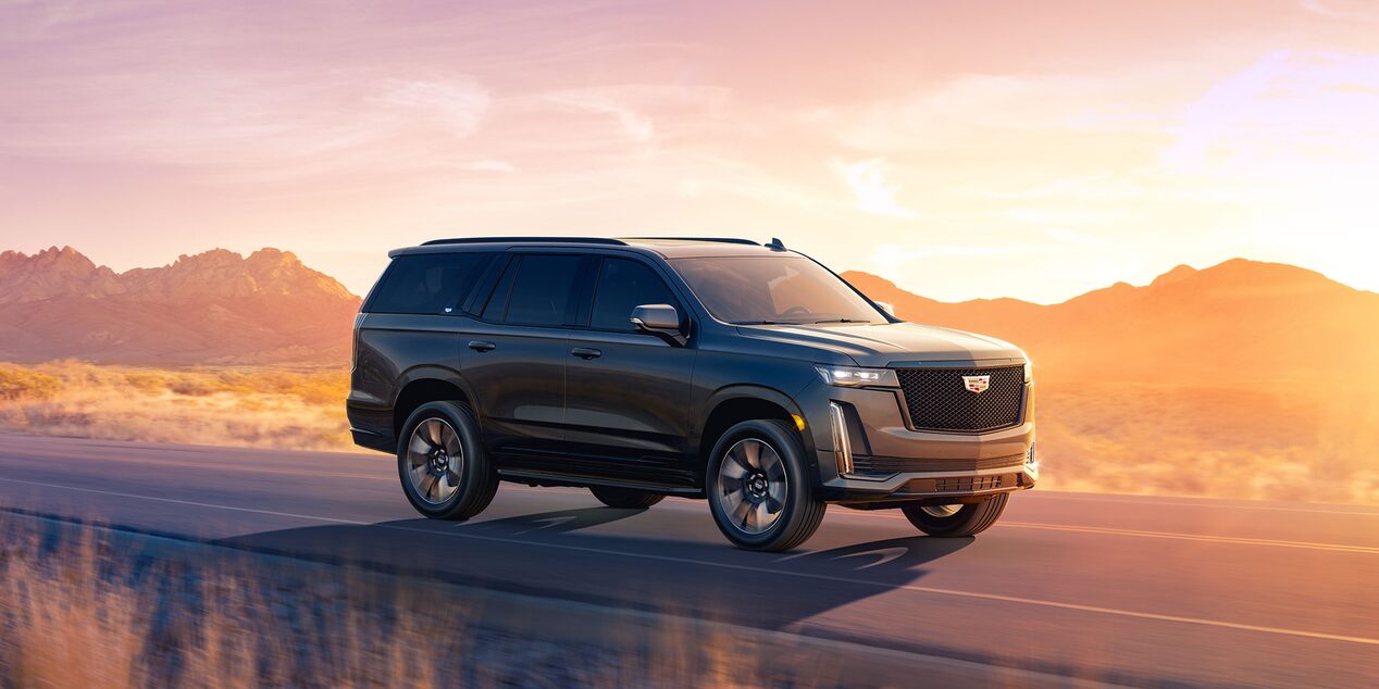 Front right view of the 2024 Escalade driving on the road during a sunset.