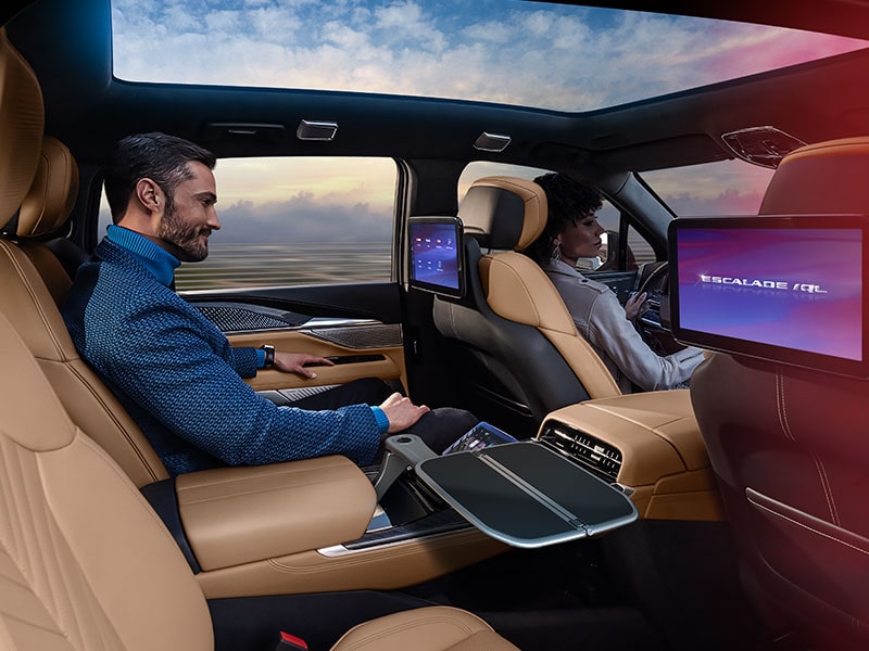 An Interior View of a Cadillac with a Man in the Back Seat Using a Tablet and a Woman Driving Showing Multiple Screens