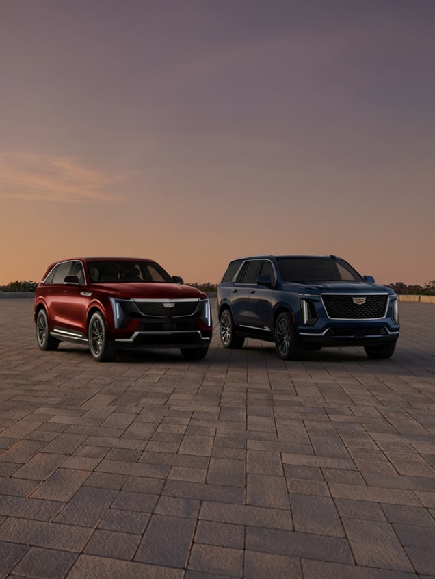 A Cadillac Escalade ICE and an Escalade IQ SUV parked side by side at sunset.
