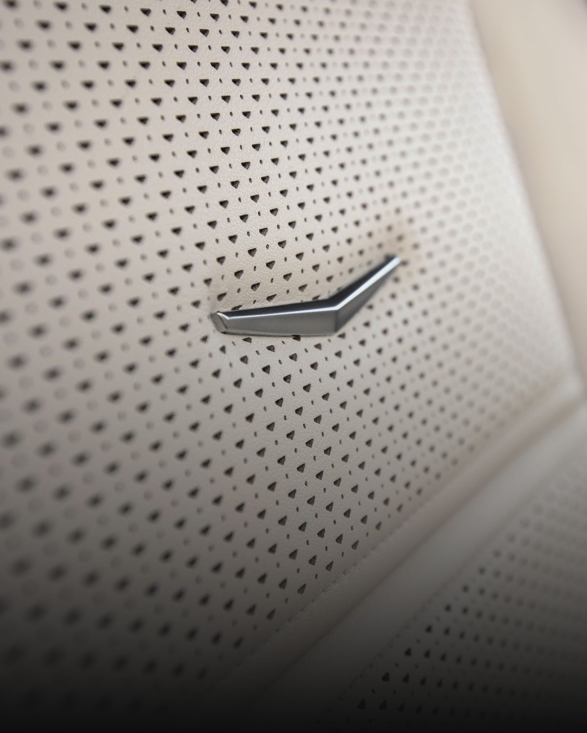 Vue rapprochée de l’écusson Cadillac en relief sur un siège en cuir perforé de couleur pâle du Cadillac Escalade 2027