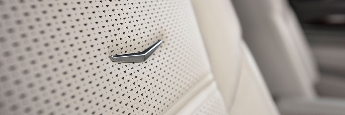 Gros plan sur l'emblème  Cadillac Crest gravé sur le siège en cuir clair perforé de l'Escalade 2027
