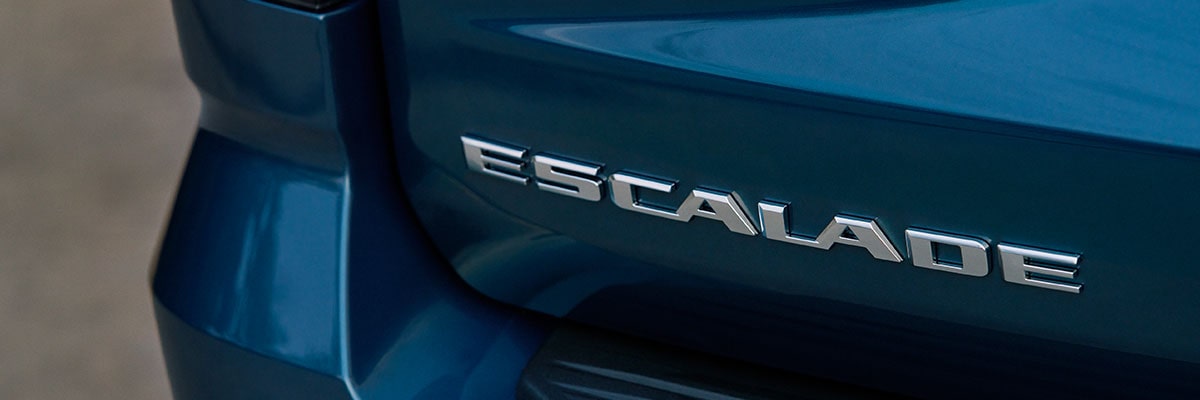Gros plan sur la plaque signalétique chromée de la Cadillac Escalade, apposée sur le hayon arrière bleu foncé