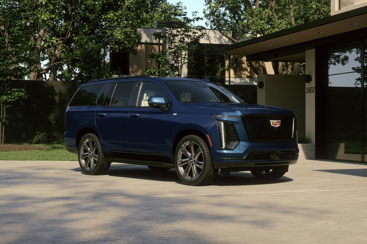 Vue de trois quarts d’un Cadillac Escalade 2027 bleu stationné devant une maison moderne
