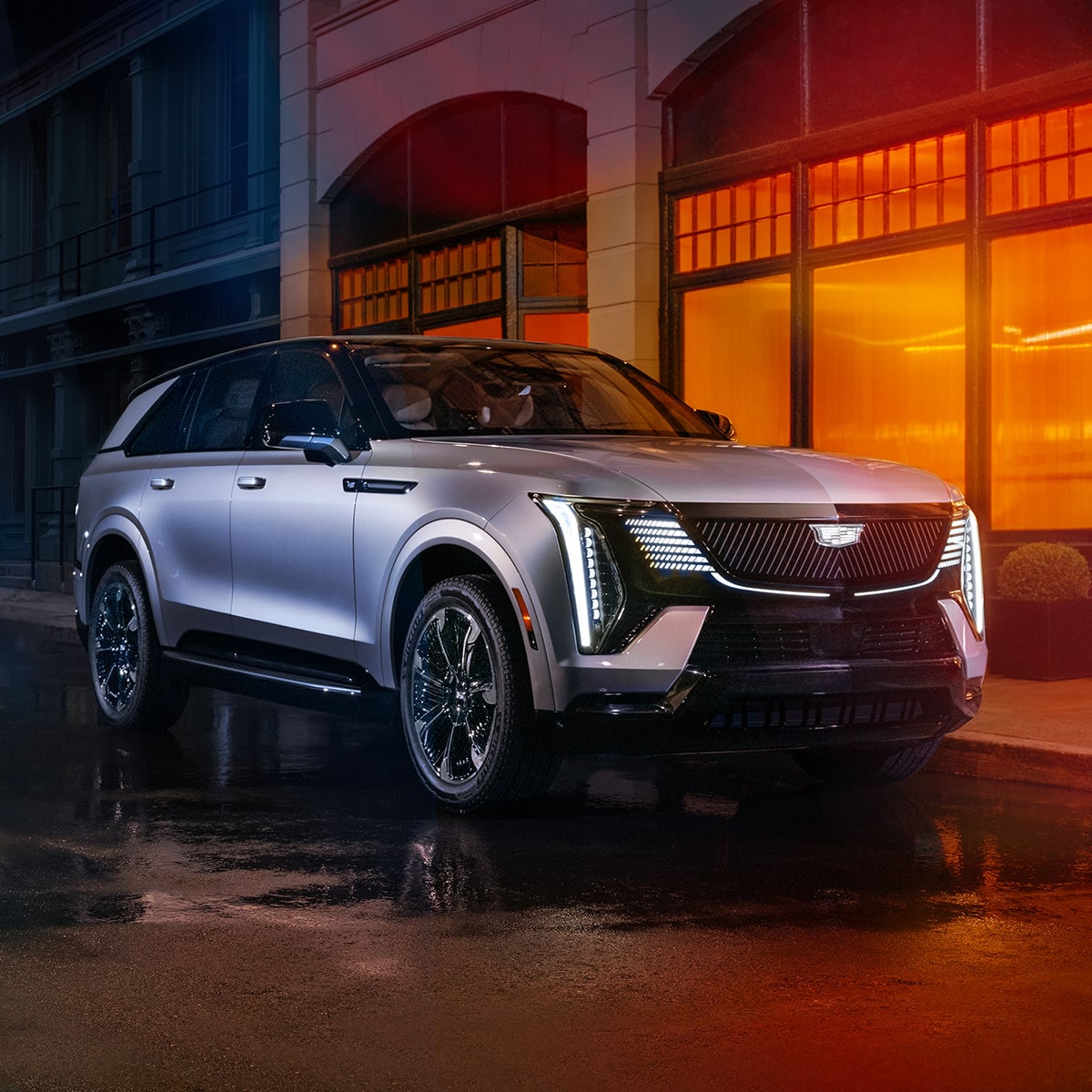 2025 Cadillac Escalade IQ electric suv parked outside a brightly-lit modern building.