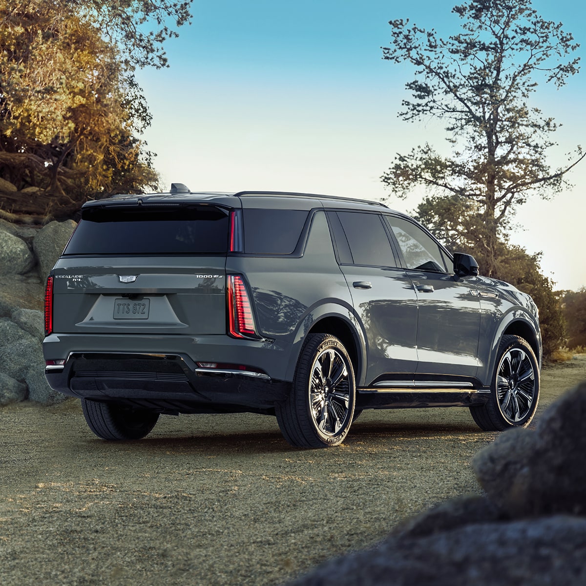 Vue latérale arrière du Cadillac Escalade IQL 2026 en mouvement dans un parc par une journée ensoleillée.