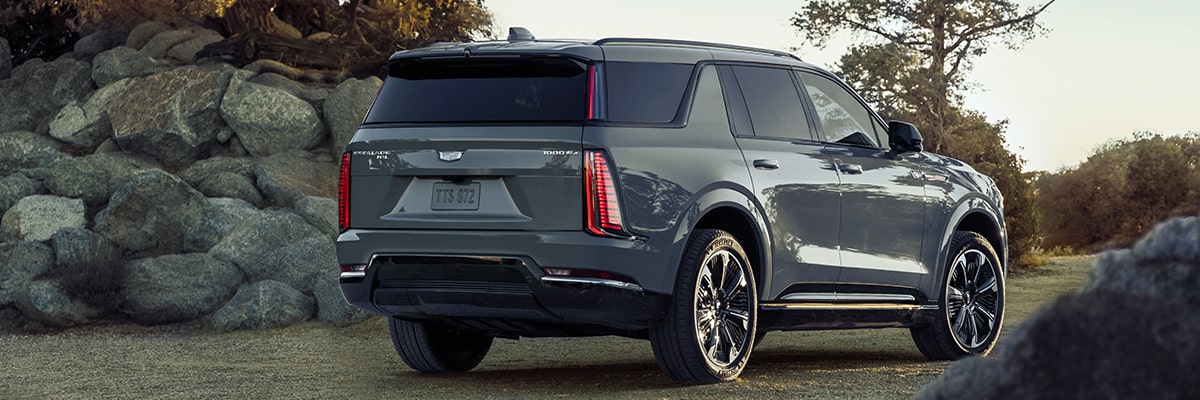Vue latérale arrière du Cadillac Escalade IQL 2026 en mouvement dans un parc par une journée ensoleillée.
