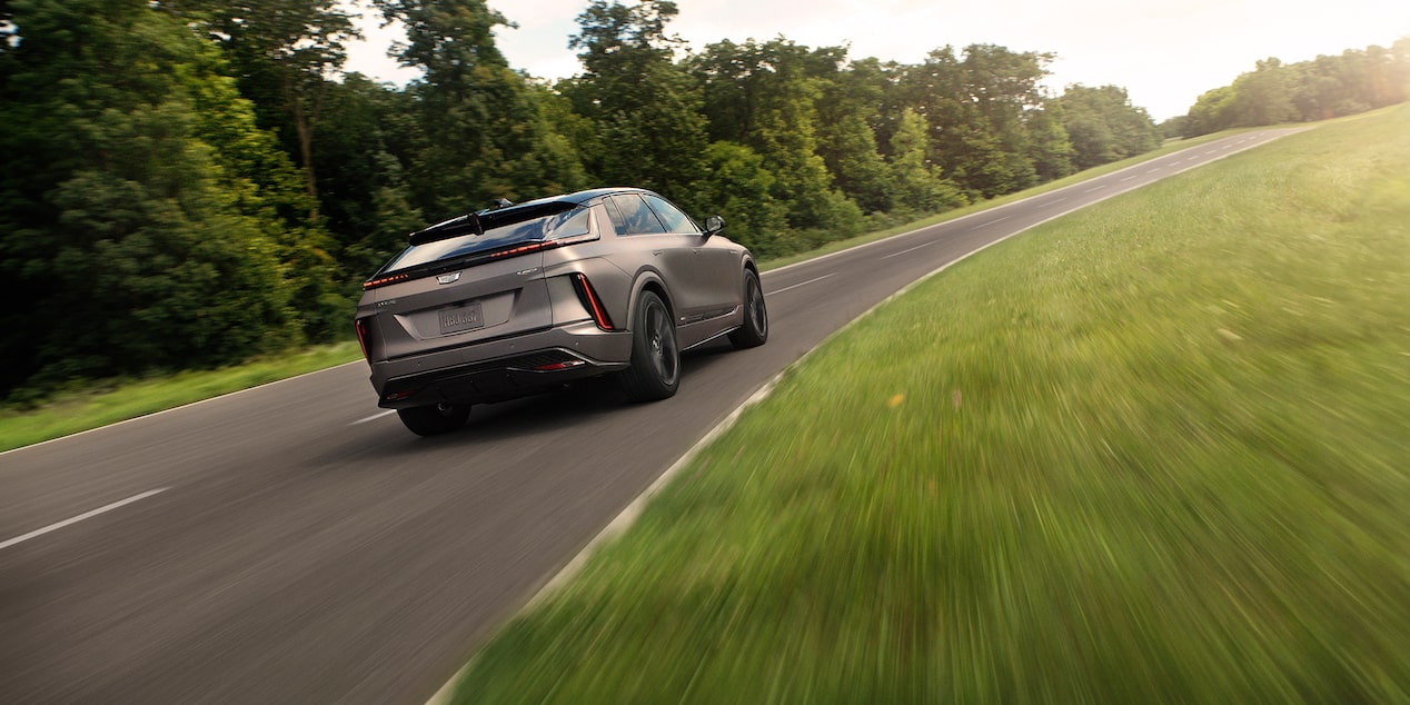 Back-side view of the 2026 Cadillac LYRIQ-V driving alone on a tree-lined road.