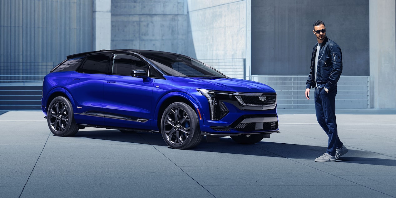 Side profile of the 2025 Cadillac OPTIQ-V in blue parked next to a man.