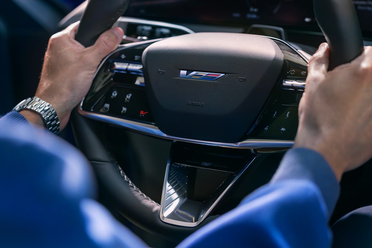 Driver gripping the Cadillac OPTIQ-V steering wheel with V-Series badge.