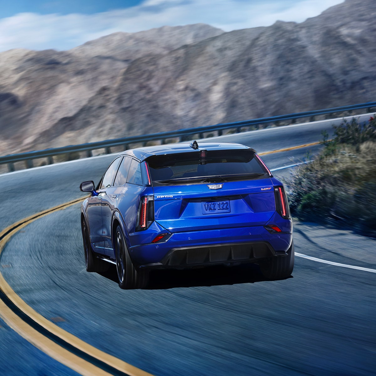 Rear view of Cadillac OPTIQ-V taking a turn on a mountain road.