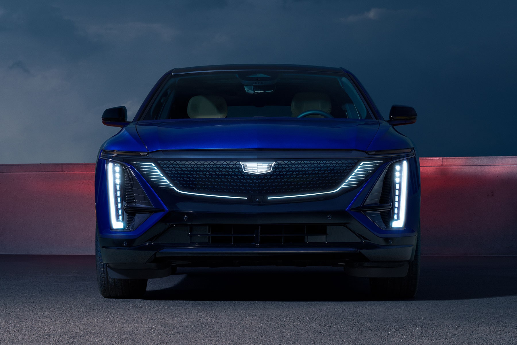Front view of a blue 2027 Cadillac LYRIQ parked at night, featuring a distinctive illuminated grille.