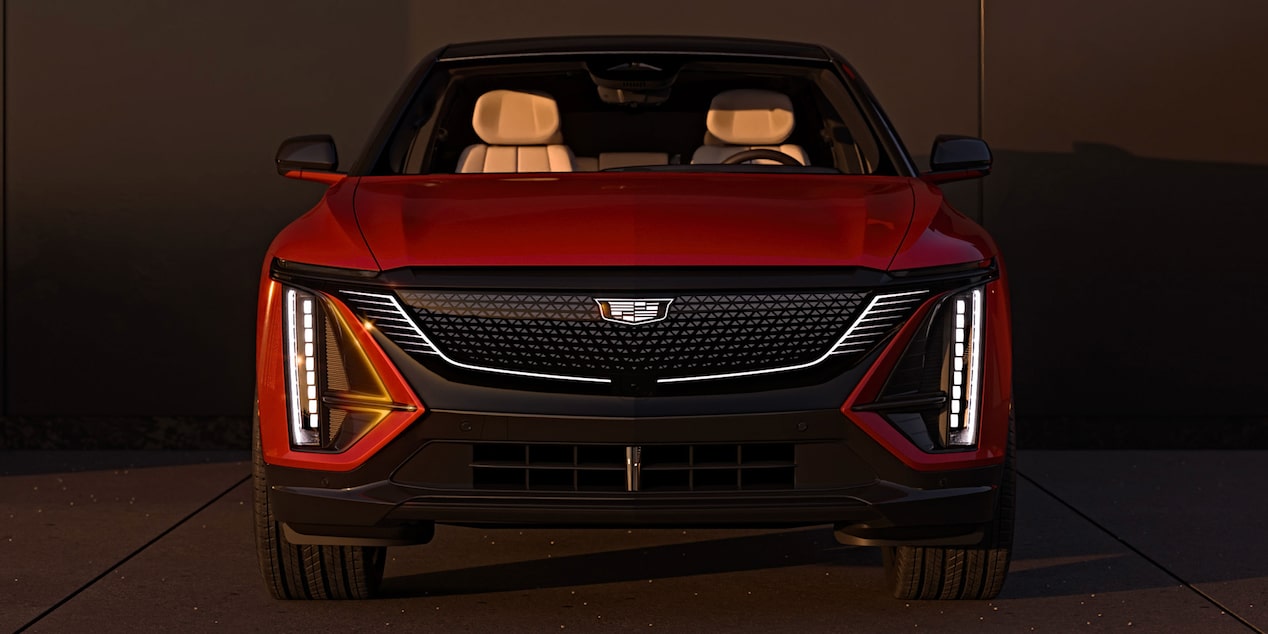 Front view of a red 2027 Cadillac LYRIQ showcasing its illuminated grille and vertical LED lighting signatures.
