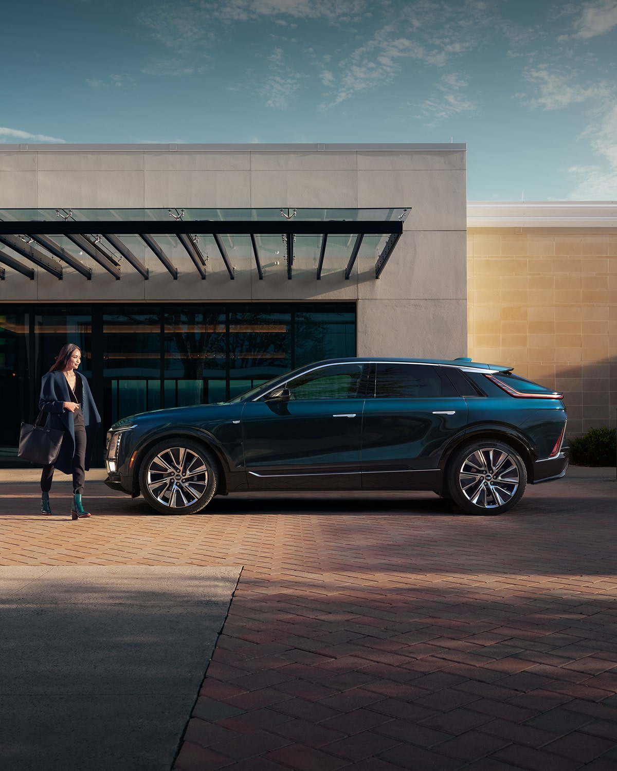 Side view of a black 2027 Cadillac LYRIQ parked outside a modern building entrance.