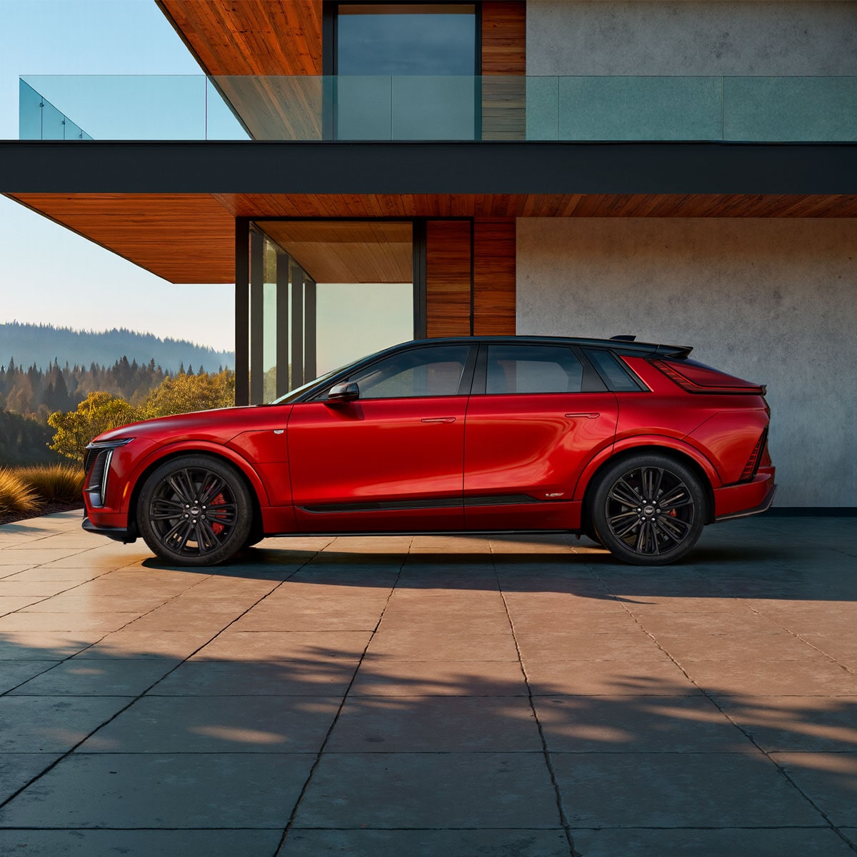 Side view of a red 2027 Cadillac LYRIQ parked outside a modern home.