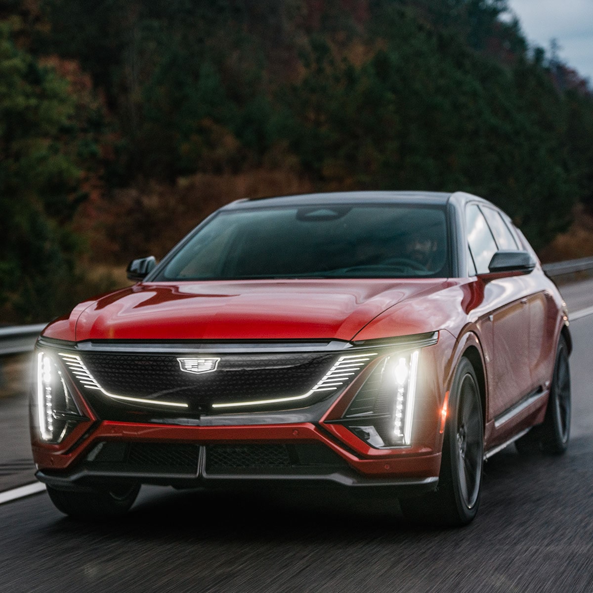 A 2027 Cadillac LYRIQ driving alone on the road with its headlights open.