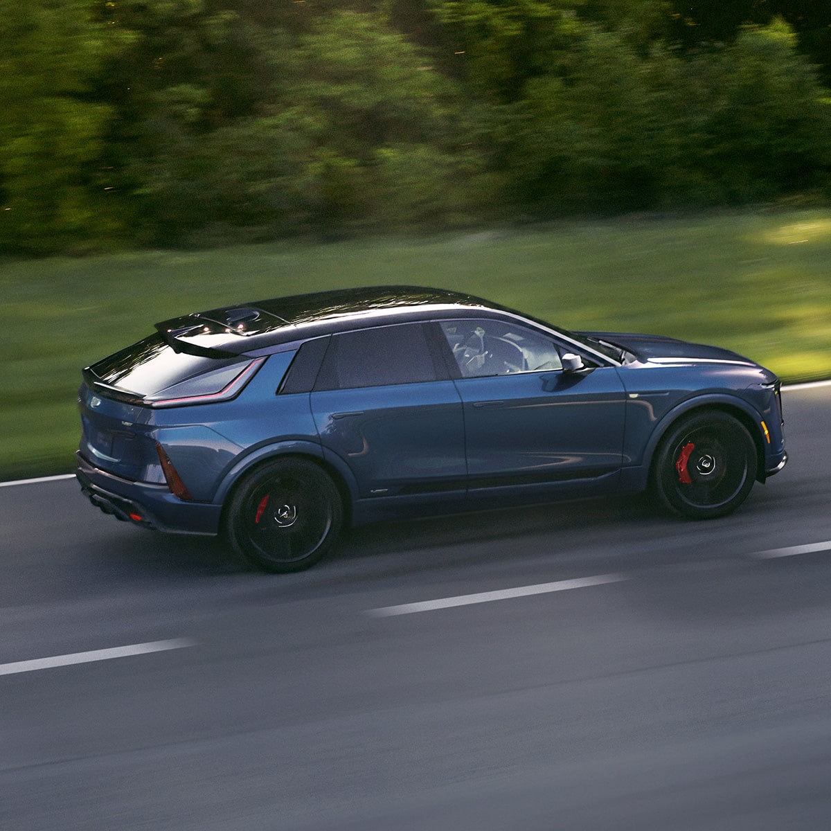 Side view of the 2027 Cadillac LYRIQ driving fast on a tree-lined road.