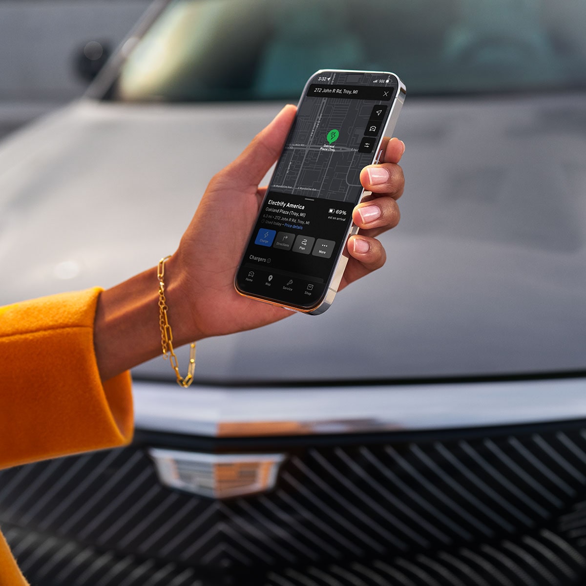 Hand Holding a Smartphone Displaying Cadillac Vehicle Controls in Front of a 2027 Cadillac LYRIQ-V.