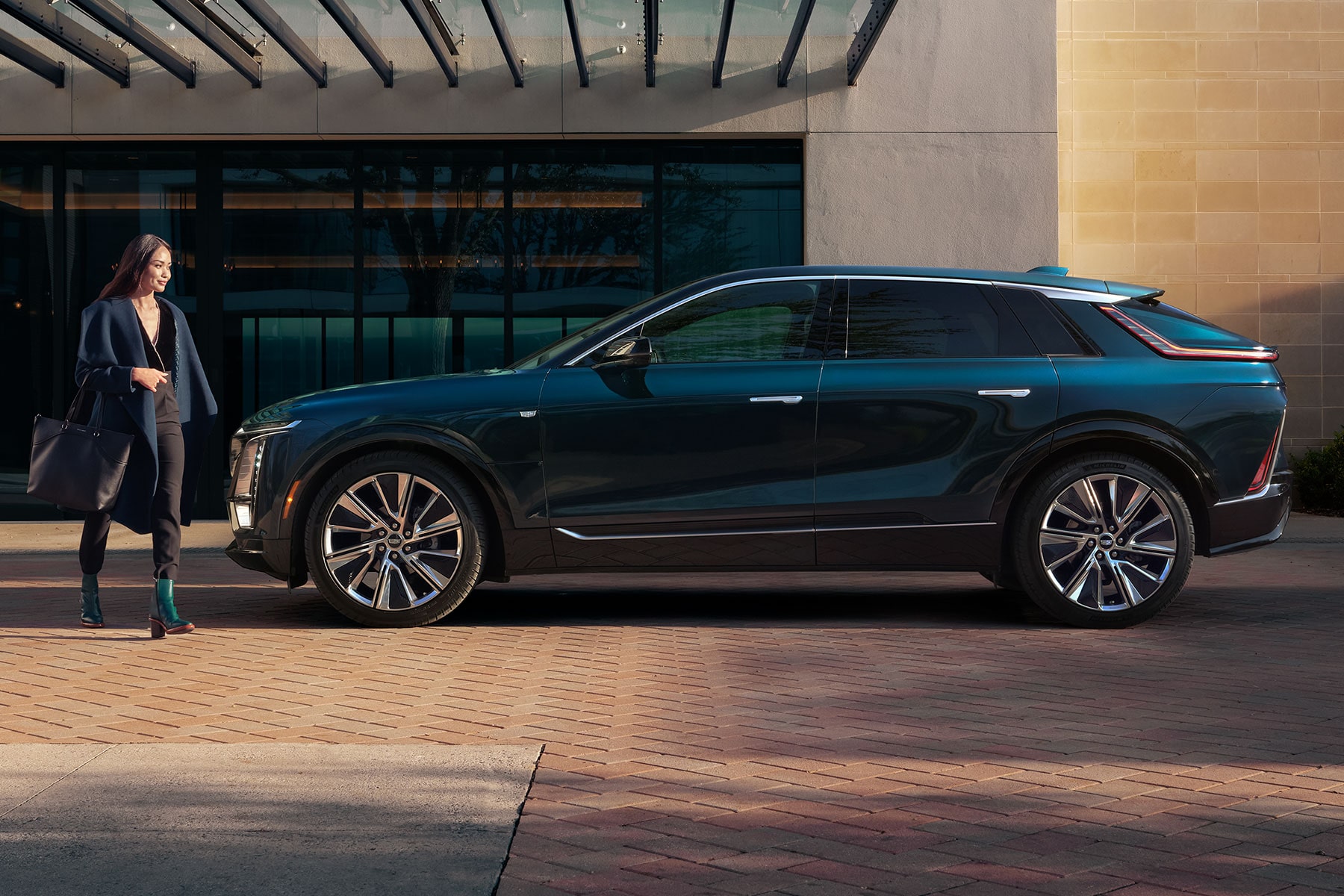 Side view of the 2027 Cadillac LYRIQ parked outside a building as person walks past it.