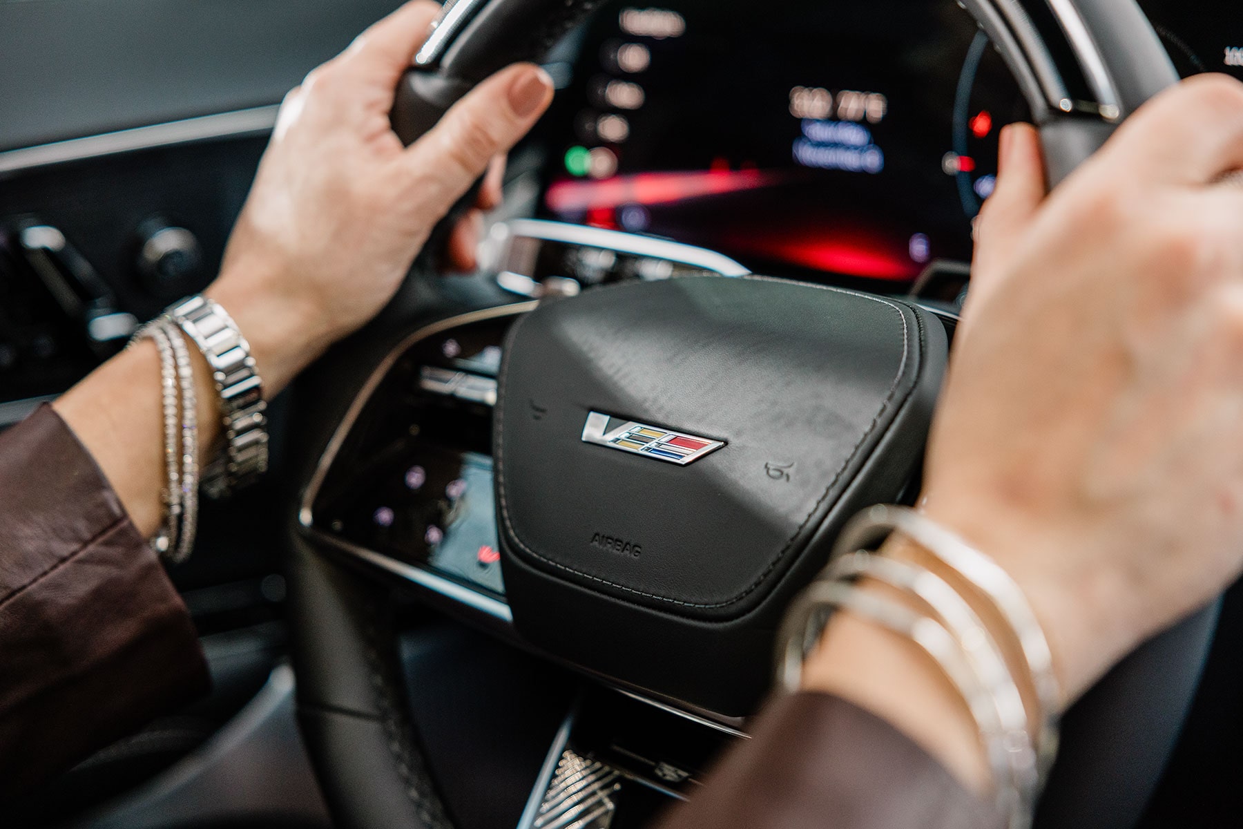 A person's hand on the steering wheel of a 2027 Cadillac LYRIQ-V.