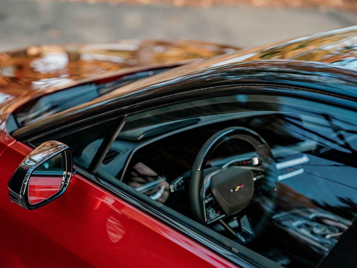 Close-up view through the side window of a red 2027 Cadillac LYRIQ-V, showcasing the premium interior and driver-focused cockpit.