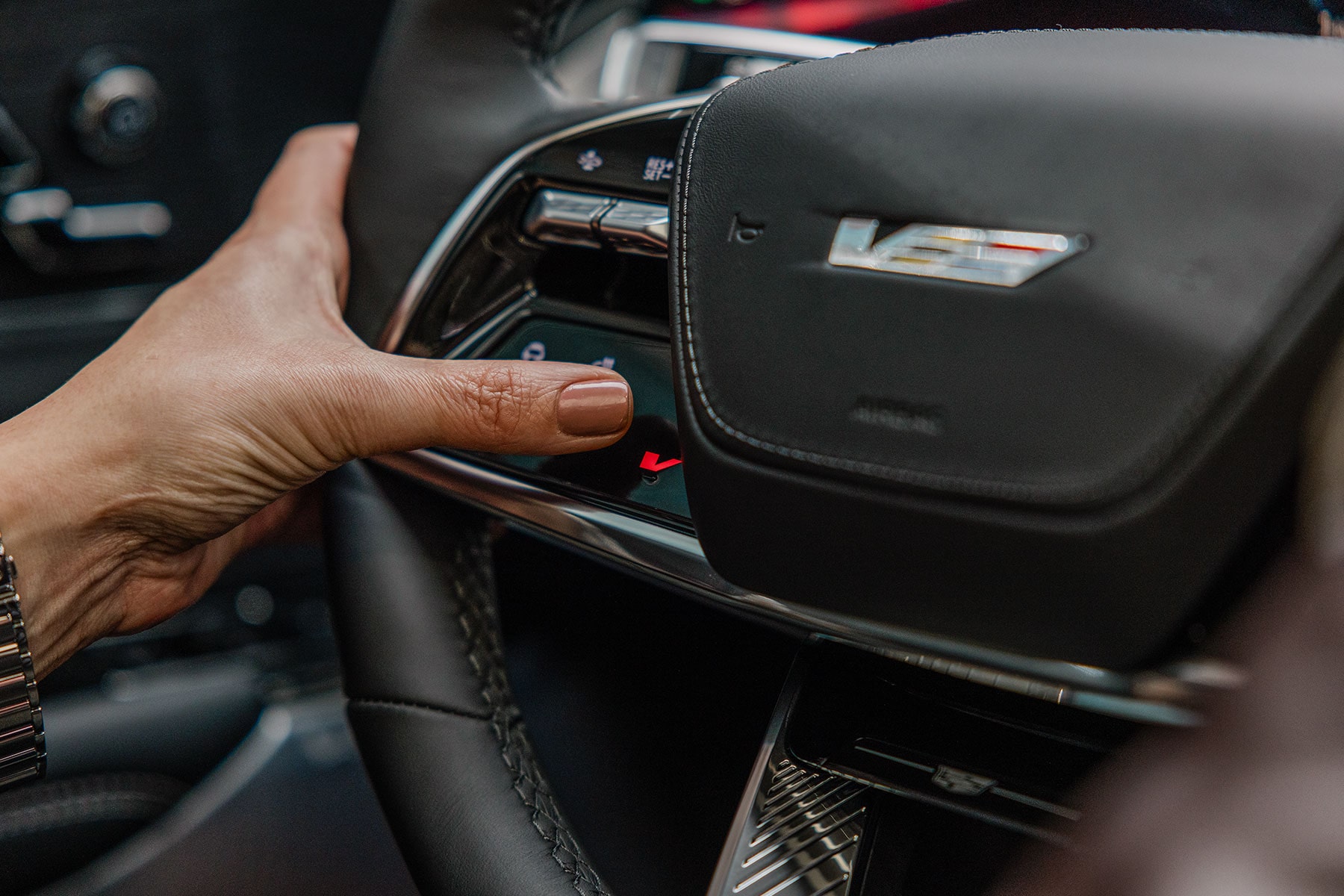 A person's hand pressing a button on the steering wheel of the 2027 Cadillac LYRIQ-V.