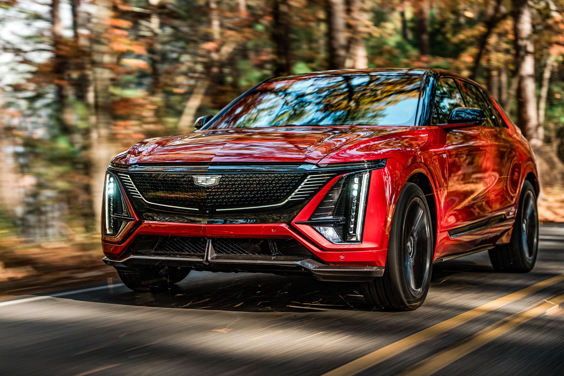2027 Cadillac LYRIQ-V driving on a tree-lined road on a sunny day.
