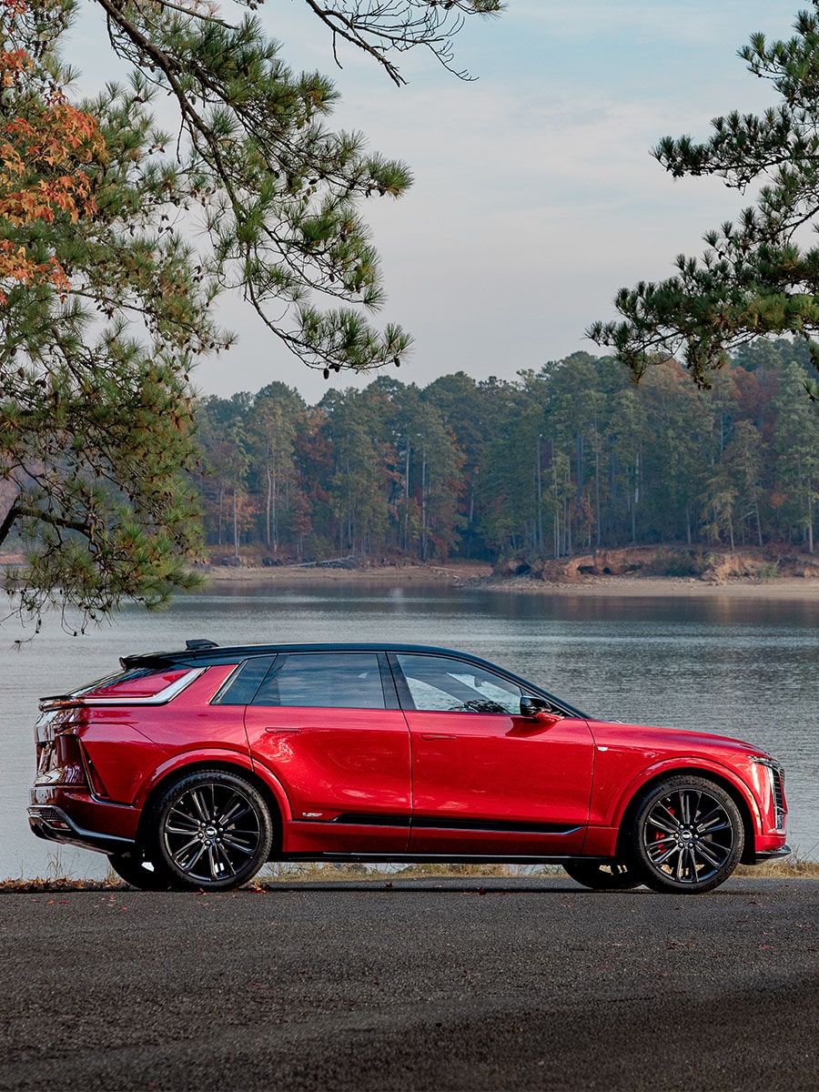 Side view of a red 2027 Cadillac LYRIQ-V parked by the lake.