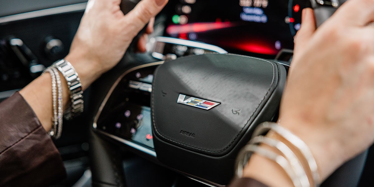 A person's hand on the steering wheel of the 2027 Cadillac LYRIQ-V SUV.