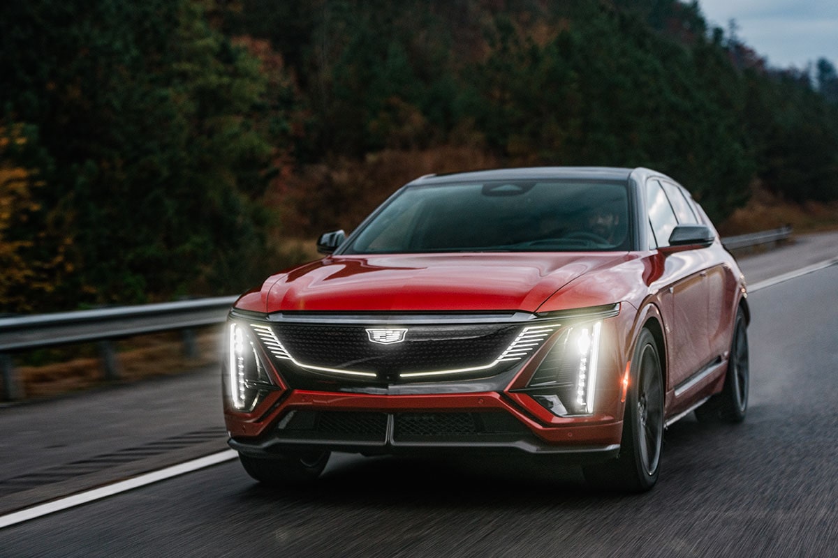 2027 Cadillac LYRIQ-V electric SUV driving on the road with its headlights on.
