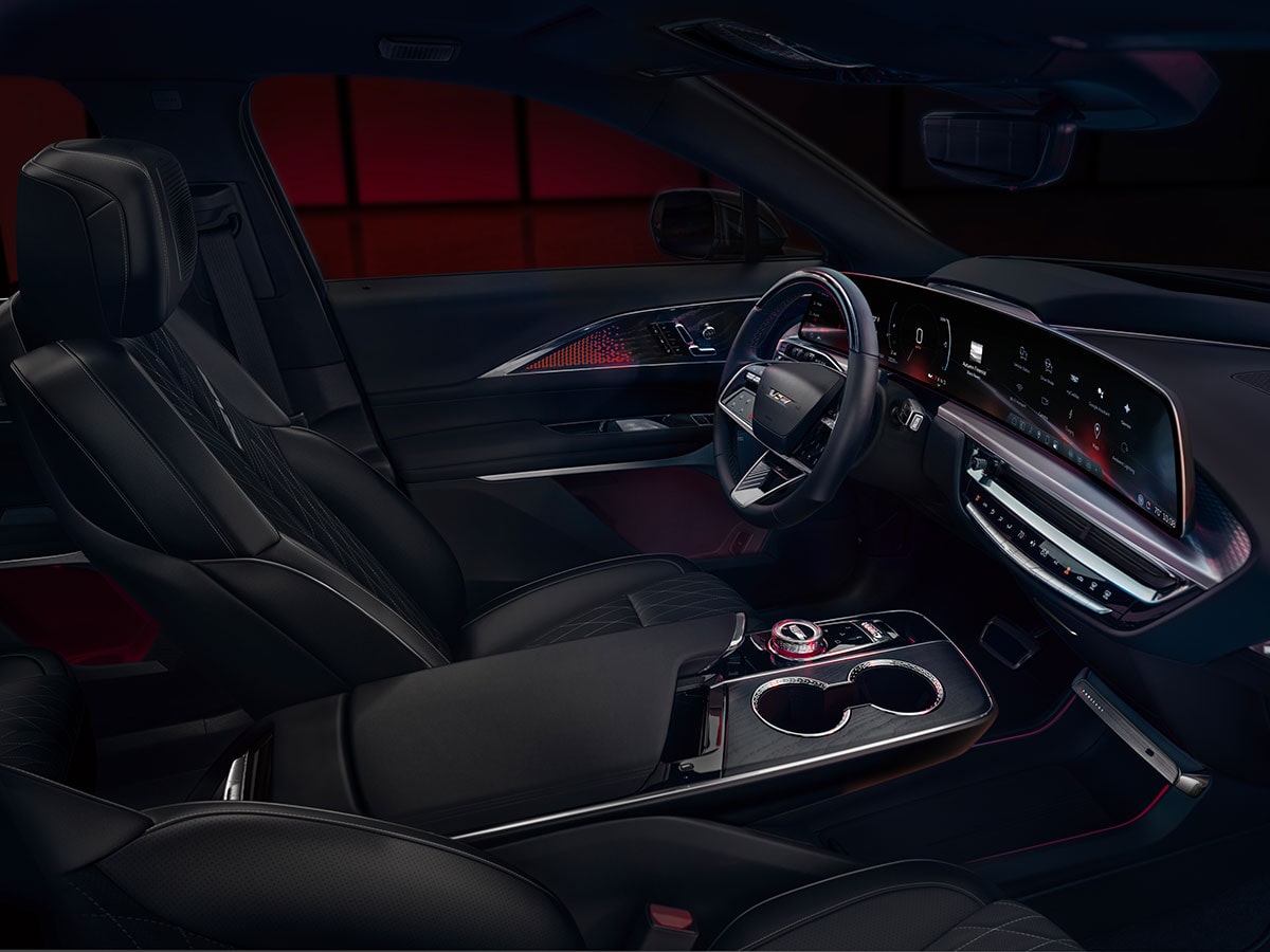 Side view of the front interiors of the 2027 Cadillac LYRIQ-V in a dimly-lit area.