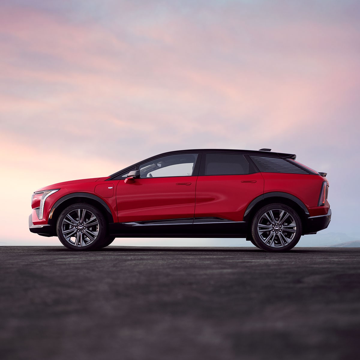 Vue de profil d’une Cadillac OPTIQ rouge 2027 sous un ciel magnifique.