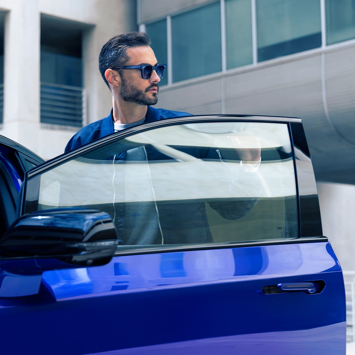 Un homme portant des lunettes de soleil à la porte du conducteur, prêt à monter dans une OPTIQ-V bleue.