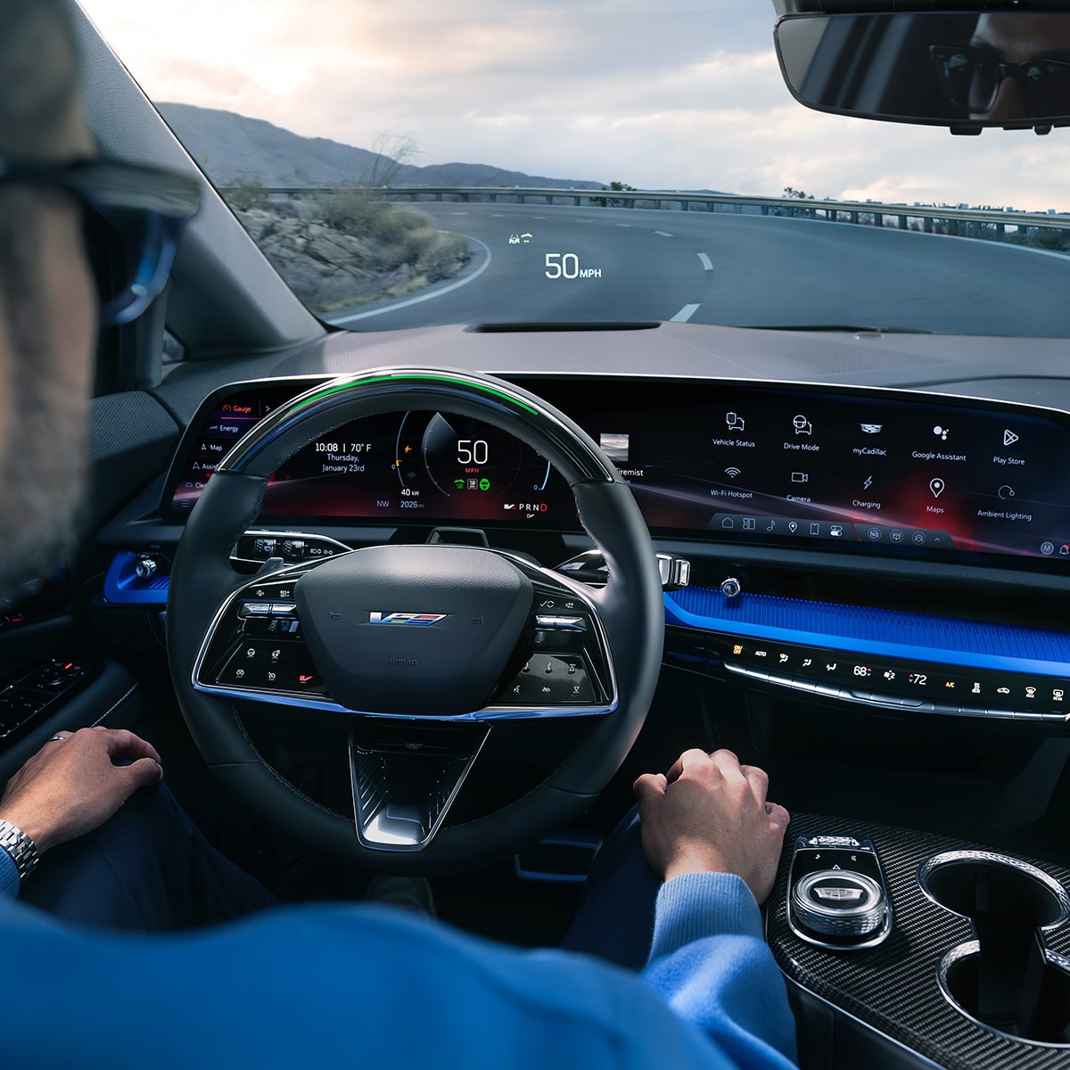 Vue du siège conducteur d’un homme conduisant l’OPTIQ-V 2027 sur une route tout en utilisant la fonction mains libres Super Cruise.