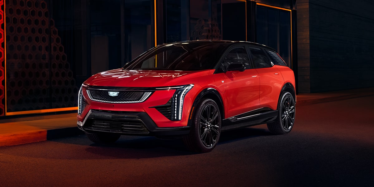 Vue aux trois quarts d’une Cadillac OPTIQ rouge 2027 stationnée dans une allée.