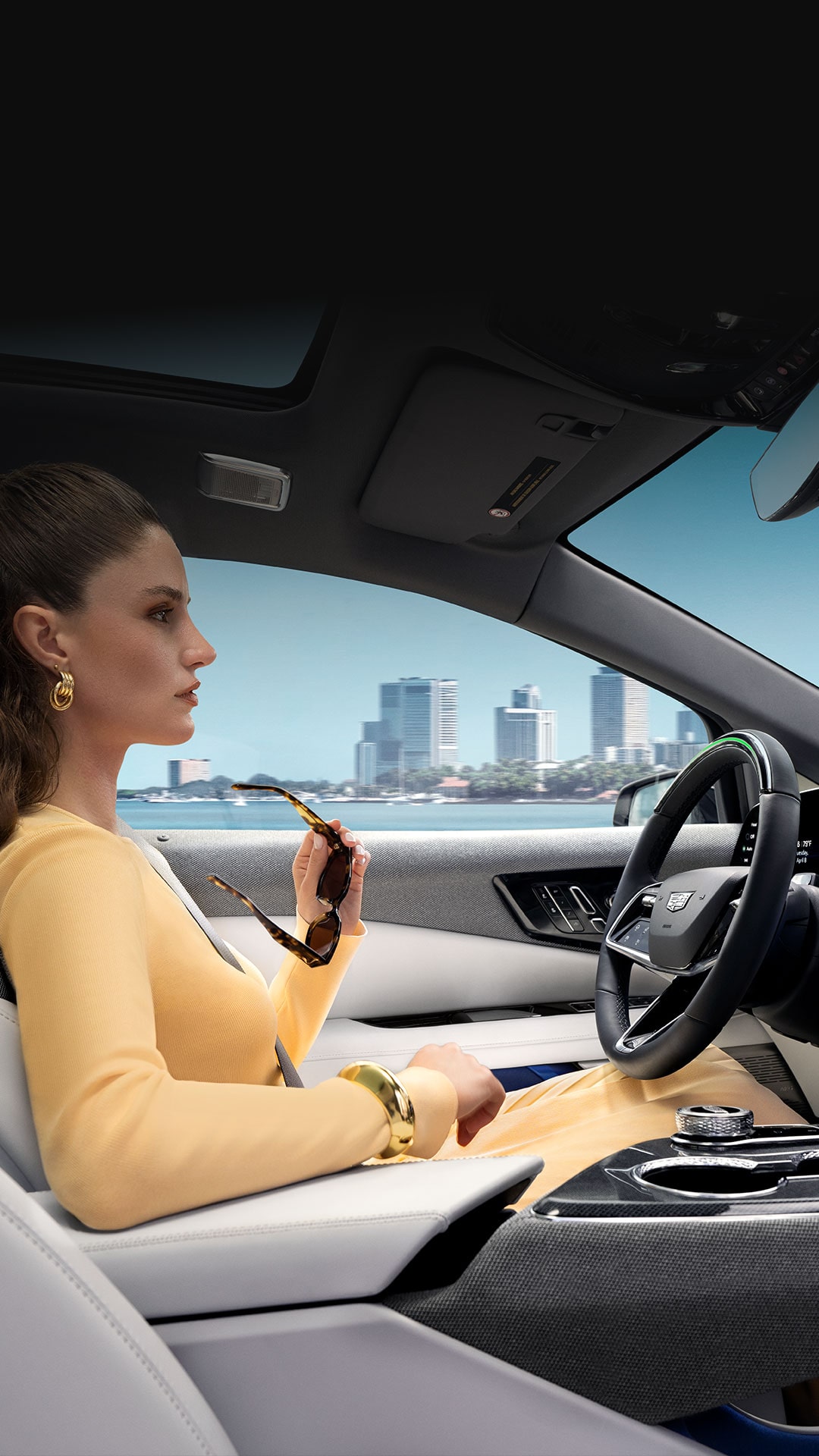 Vue passager d’une personne conduisant une Cadillac OPTIQ 2027 devant la ville en utilisant la technologie mains libres Super Cruise.