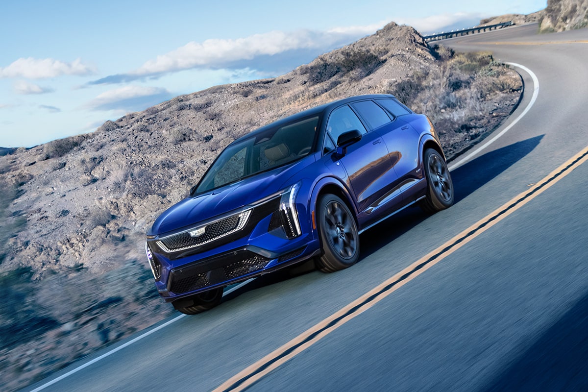 A Blue Cadillac OPTIQ-V Driving Around the Curve of a Mountain Road