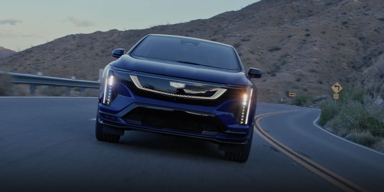 Head On View of a Blue Cadillac OPTIQ-V Driving on a Mountain Road with the Headlights On