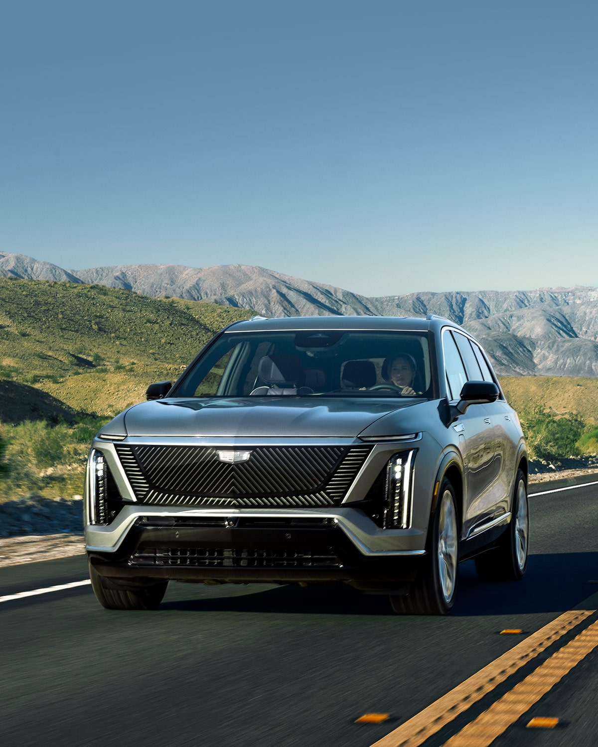 The 2027 Cadillac VISTIQ 3-row Electric SUV Driving Down a Road in the Mountains.
