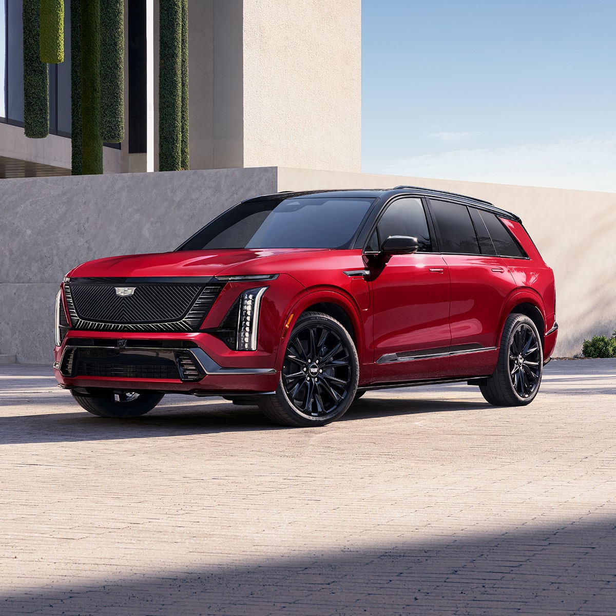 Vue aux trois quarts d’un SUV électrique VISTIQ 3 rangées 2027 garé près d’un mur en béton.