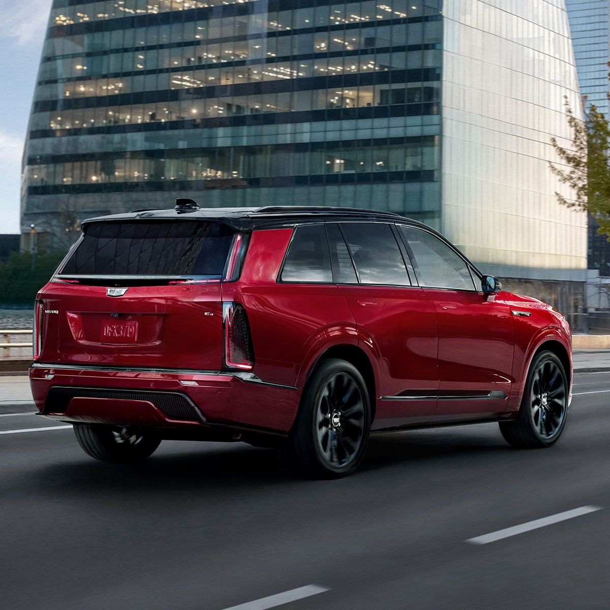 Une vue arrière aux trois quarts d’une Cadillac VISTIQ rouge 2027 roulant dans une rue urbaine.